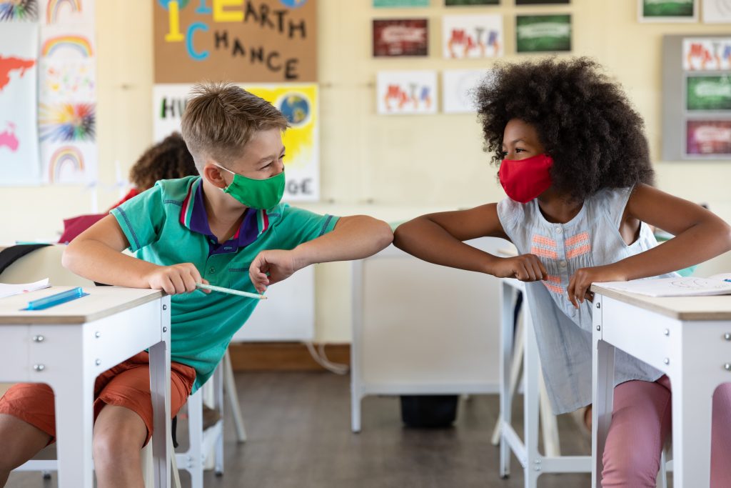 Two children in school wearing masks shaking elbows