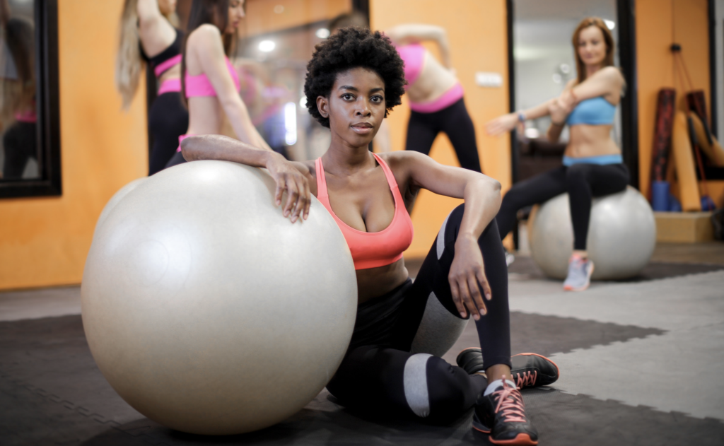 Woman with fit ball sitting on floor while training in modern gym
