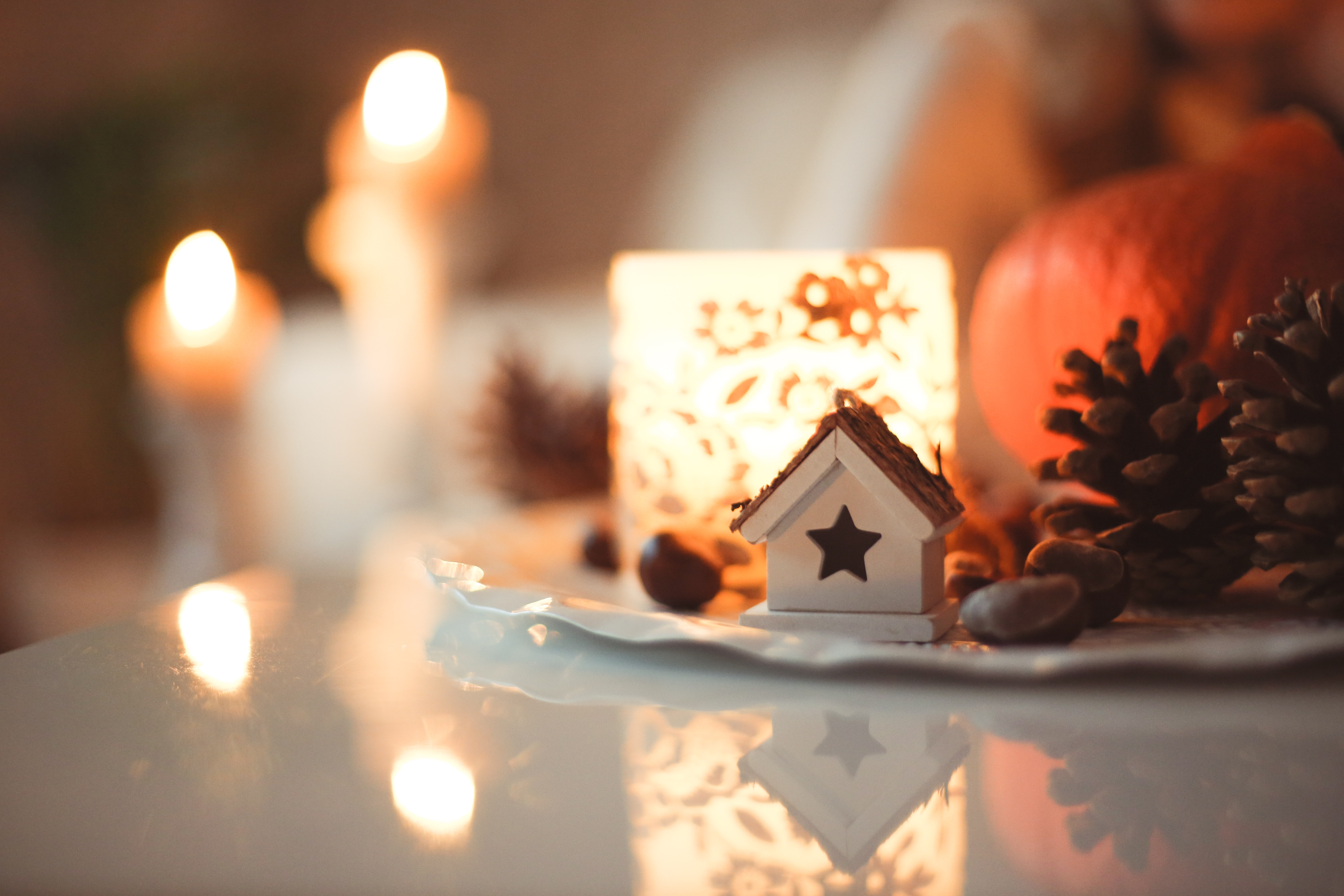 White ceramic house, grouped with pinecones and backlit by a candle