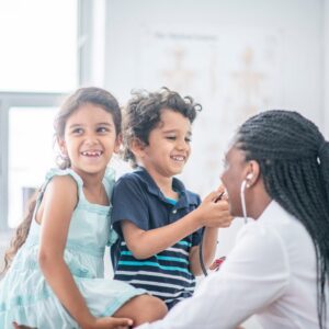 Doctor supporting two children during a medical visit, representing pediatric Long COVID care and awareness.