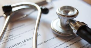 Close up of a stethoscope resting on medical paperwork and a health care bill.