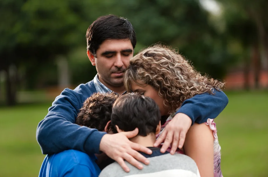 Two adults and two children sharing a hug outdoors.