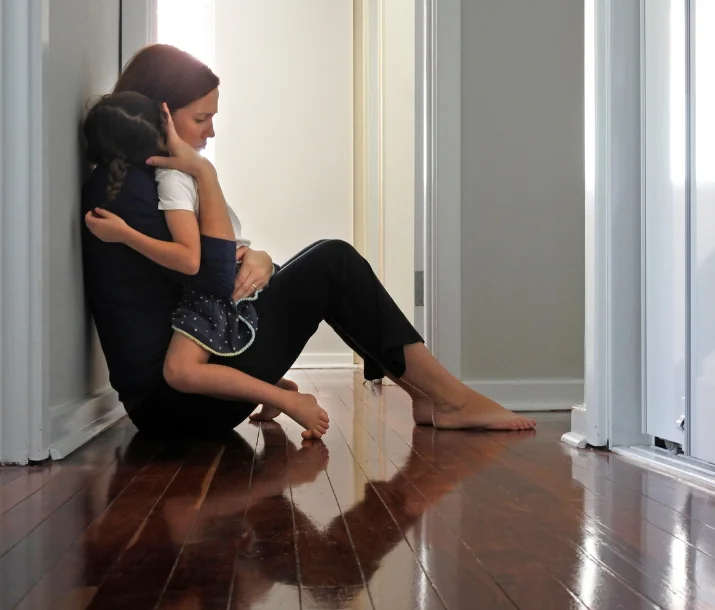 An adult sitting on the floor and holding a child.