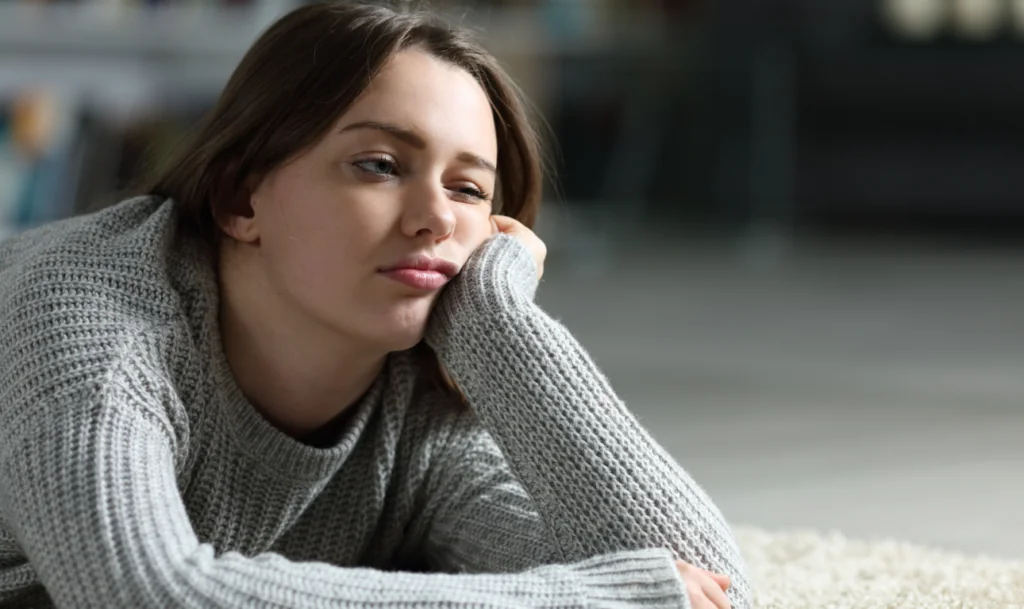A young person in a gray knitted sweater reclining with their cheek resting on one hand.