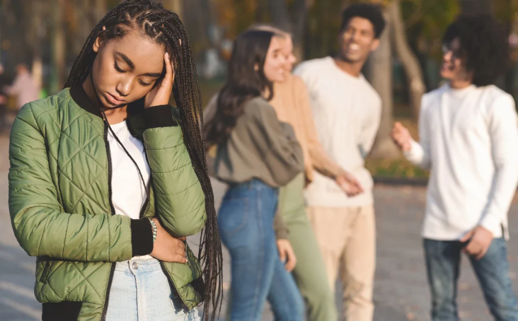 A young person holding their head and abdomen while others talk in the background.