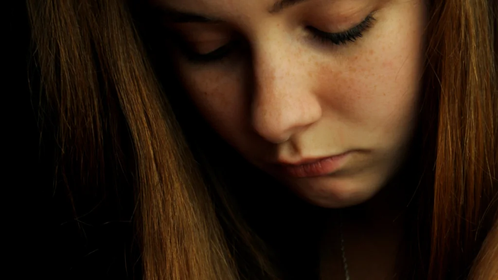 A young person with long brown hair looking down.