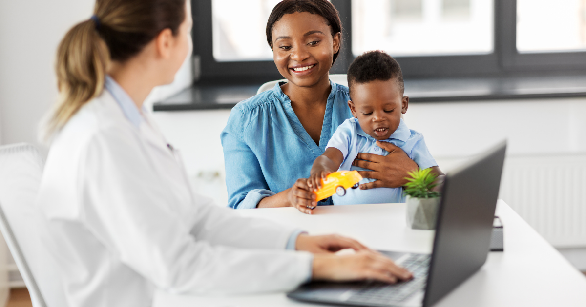 A parent and young child meet with a clinician at a desk.