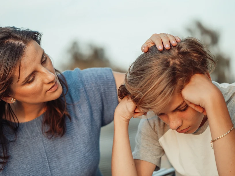 An adult comforting a child with their head lowered.
